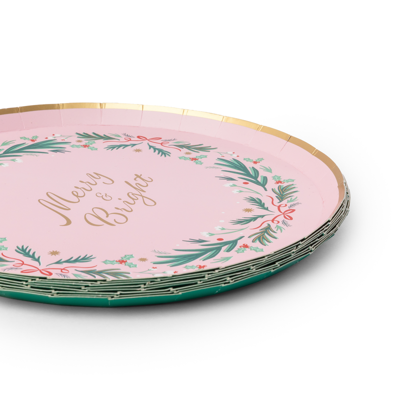 Angled stack of pink Christmas plates showing the green wreath, gold "Merry & Bright" lettering, and gold rim.