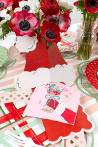 Styled holiday party table showing the pink retro cocktail napkin resting near a red floral centerpiece and holiday gifts.