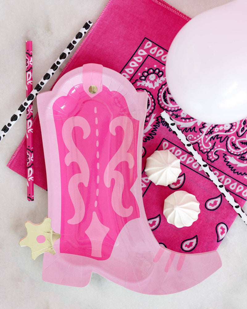 Pink cowgirl boot paper plate styled flat lay on hot pink bandana with cow print straws, pink paisley straws, pink balloon, and meringue cookies for a Nashville bachelorette tablescape