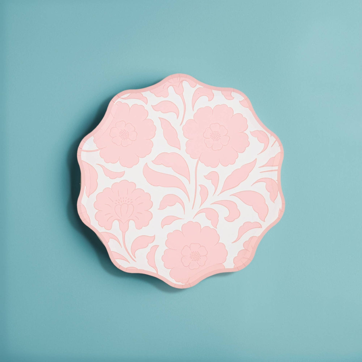 Single pink block-print floral scalloped paper plate on a blue background.