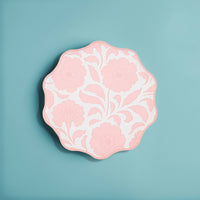 Single pink block-print floral scalloped paper plate on a blue background.