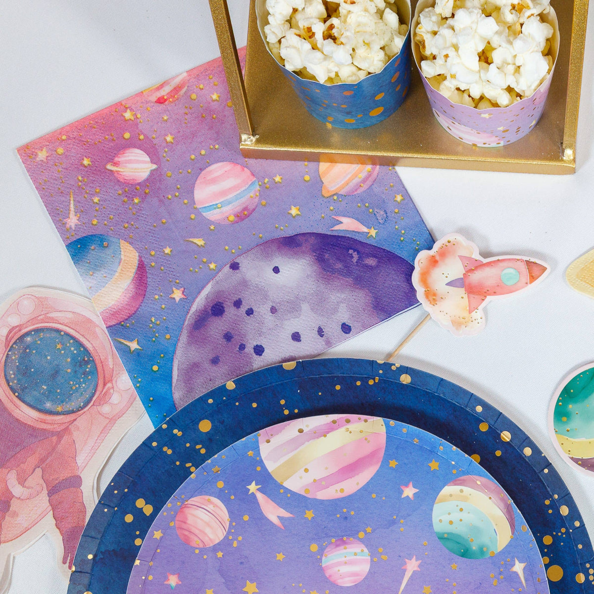 Pink space party dessert table with galaxy napkins, planet plates, popcorn cups and an astronaut cutout