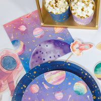 Pink space party dessert table with galaxy napkins, planet plates, popcorn cups and an astronaut cutout