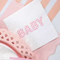 Close view of a pink gingham BABY paper napkin on a pink striped runner, napkins sold separately from the charger shown