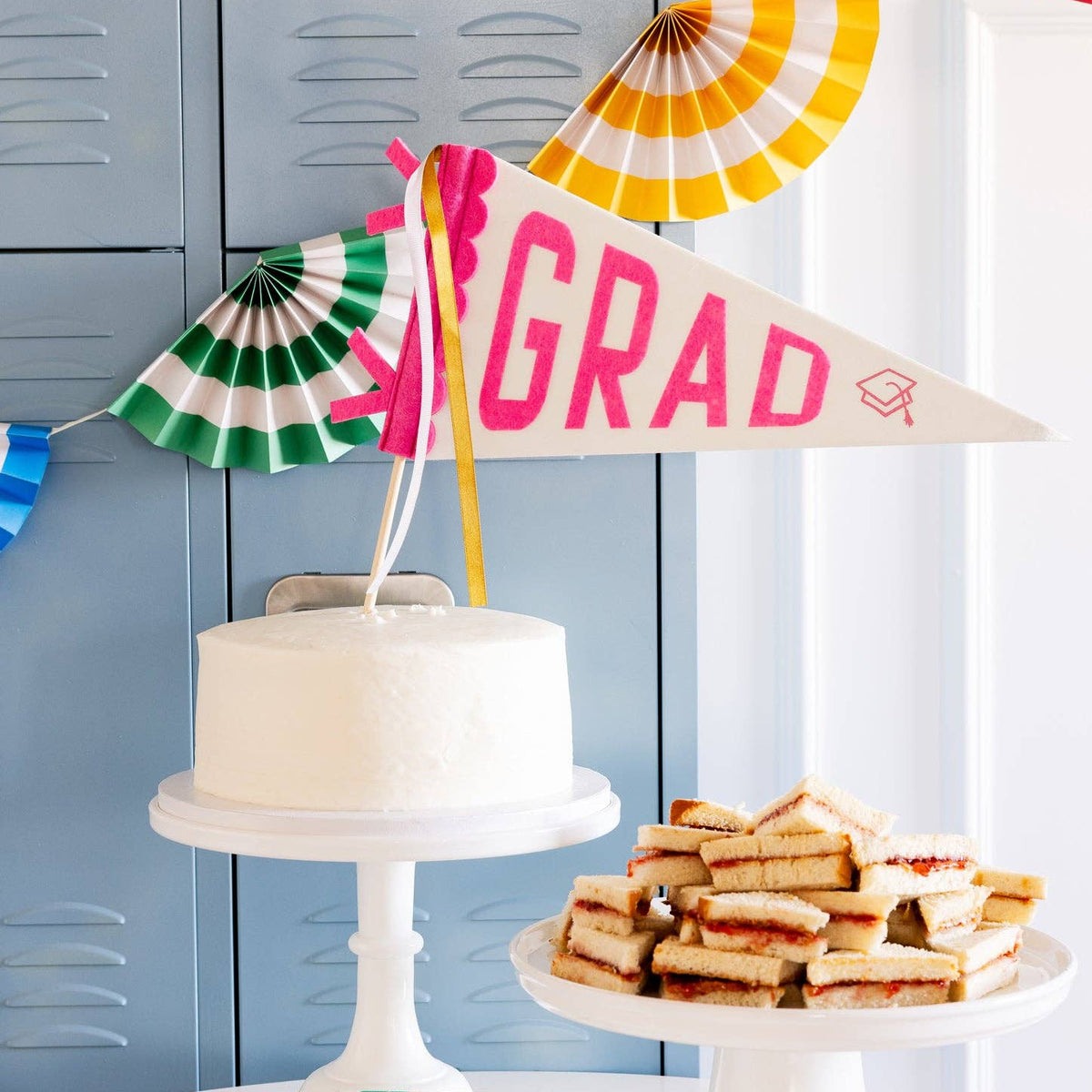 A pink felt grad pennant used as a cake topper on a white cake for a preppy pink grad theme brunch.