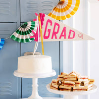 A pink felt grad pennant used as a cake topper on a white cake for a preppy pink grad theme brunch.
