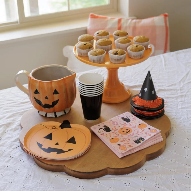 Pink Halloween napkins with black cats and pumpkins styled with jack-o-lantern shaped paper plates on a fall breakfast table with pumpkin muffins