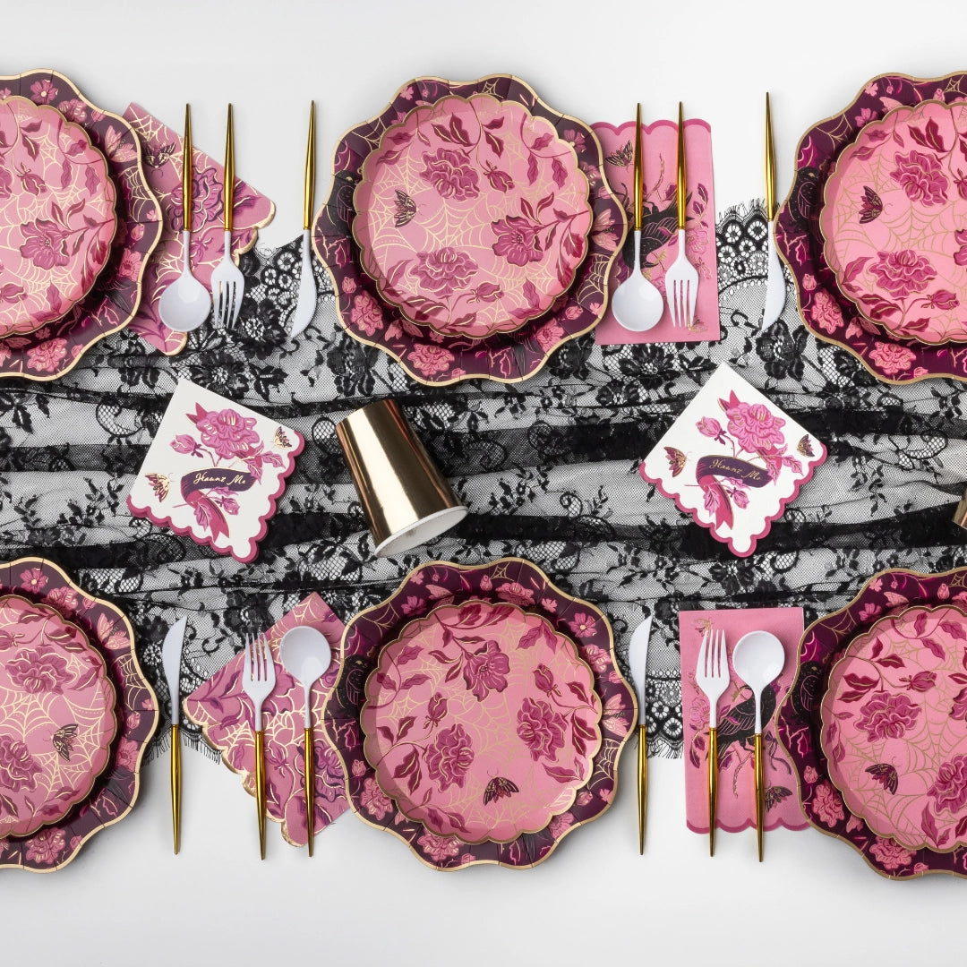 Pink and burgundy Halloween tablescape with gold-spiderweb floral plates, "Haunt Me" scalloped napkins, gold cutlery, gold cups, and a black lace runner.