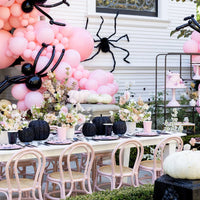 Outdoor pink Halloween tablescape with a pink balloon garland, black spiders, black pumpkins, and place settings.