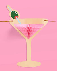 Close-up of single pink martini glass banner piece with pink honeycomb tissue and green olive detail