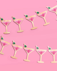 Two rows of pink martini glass banners with gold foil silhouettes and pink tissue accordions against pink background