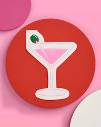 Single pink martini glass shaped cocktail napkin styled on a red plate with pink background