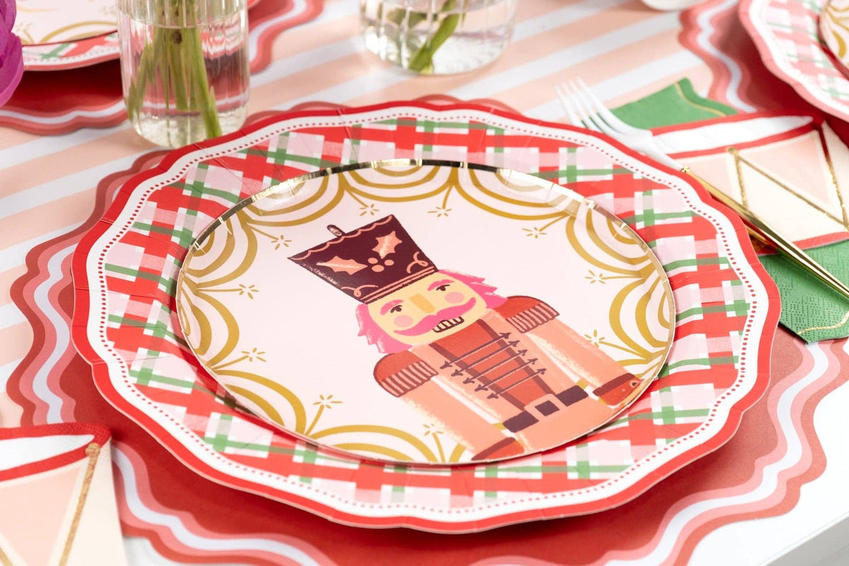 Place setting with a pink nutcracker salad plate on the plaid dinner plate over a red scalloped charger.