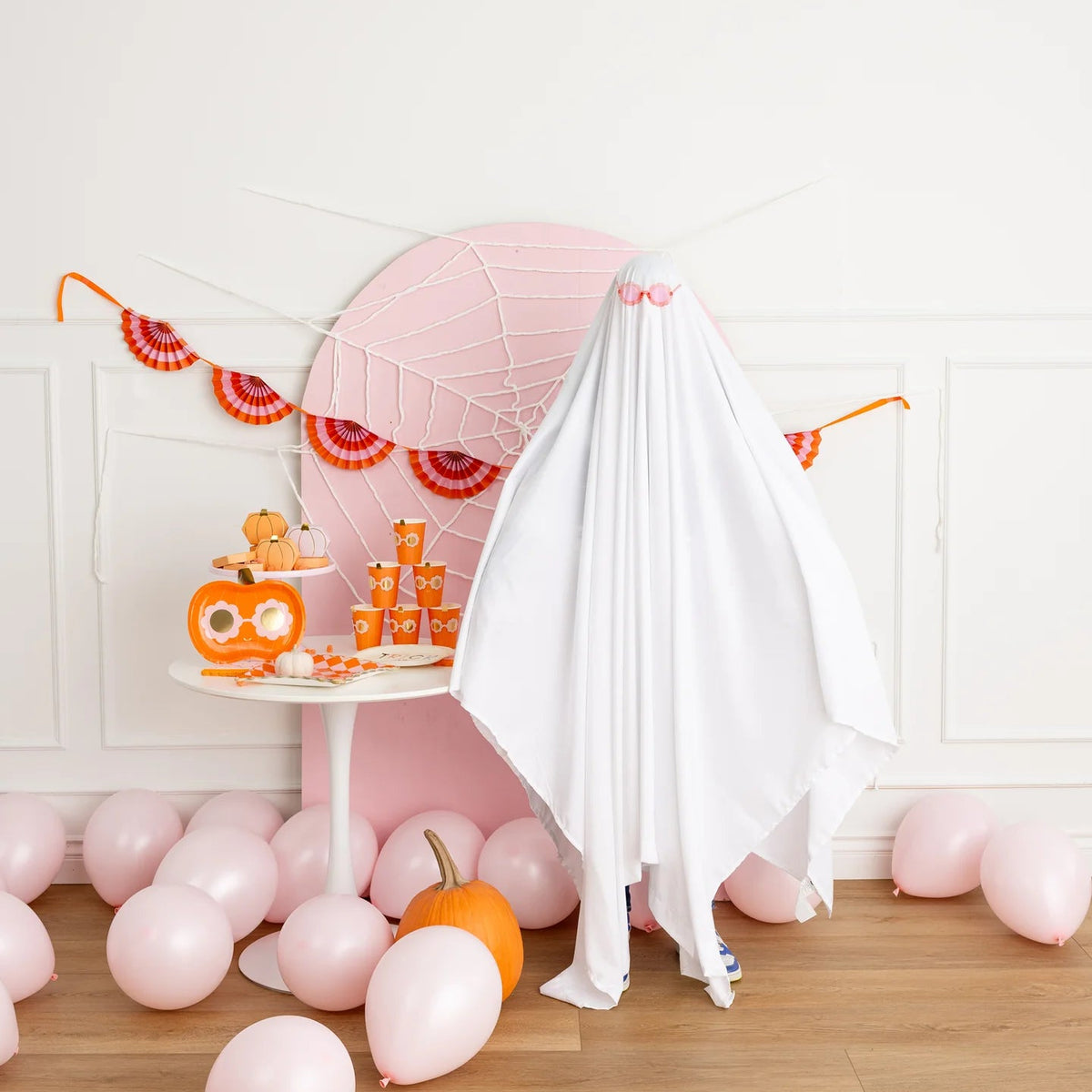 Banner strung across a pink spider-web backdrop with a child in a ghost costume.
