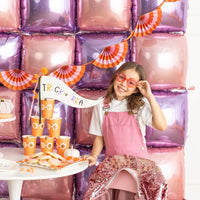 Girl at a dessert table in front of a pink and purple balloon wall with the fan banner hung across.