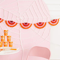 Closeup of the pink and orange accordion fans tied to ribbon on a pink spider-web board.