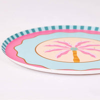 Angled close-up of a pink palm tree dessert plate with the hot-pink palm, gold flecks, and teal striped edge.