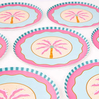 Pink palm tree paper dessert plates angled in a group, showing the wave scallop border and striped rim.