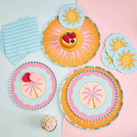 Pink palm tree dessert plate styled in a summer flatlay with an orange sunburst plate, sun napkins, and striped napkins.