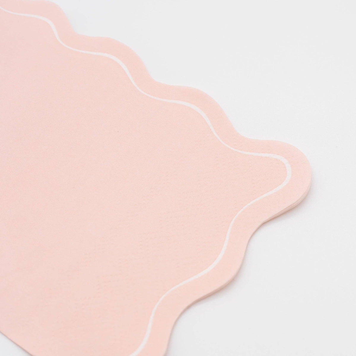Folded pink paper guest towel showing the blush tone and flowing scalloped edge from a second angle.
