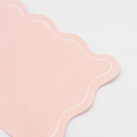 Folded pink paper guest towel showing the blush tone and flowing scalloped edge from a second angle.