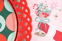 Macro crop of the pink retro cocktail napkin showing the red-gloved hand, candy cane, and shimmering foil starbursts.