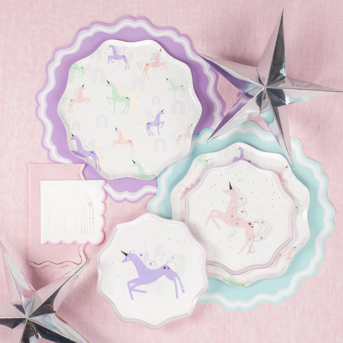 Flat lay: napkins beside layered pastel chargers and silver stars.