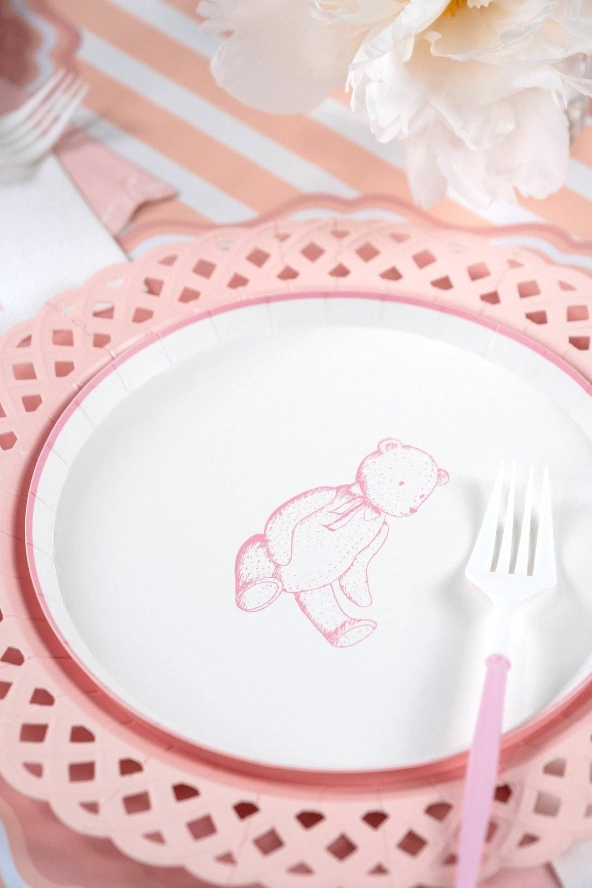 Pink teddy bear plate on a pink charger over a peach striped runner with white peonies