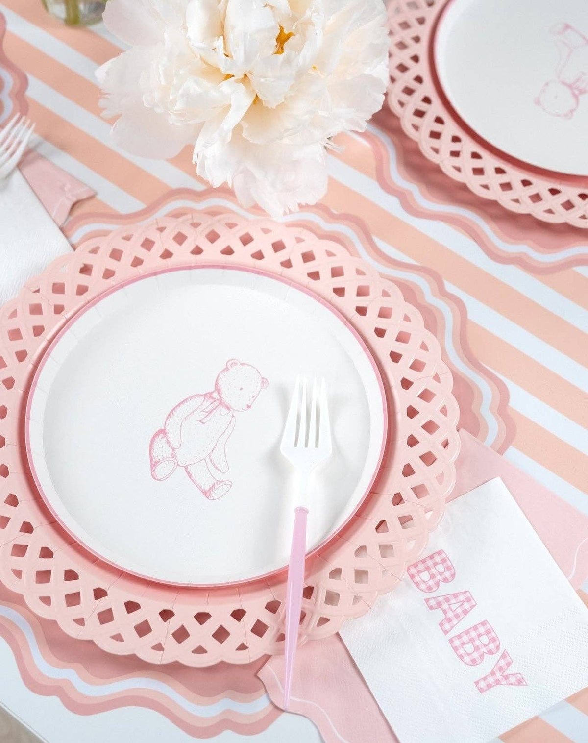 Two pink teddy bear plate settings on pink lattice chargers with white peonies and a striped runner