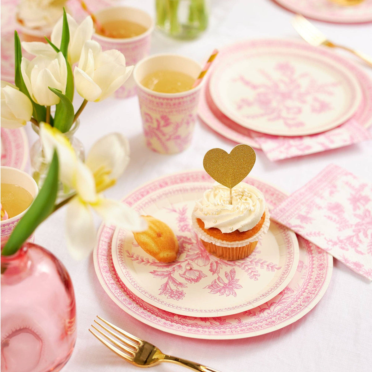 Tea party table setting with pink toile plates and cupcakes.