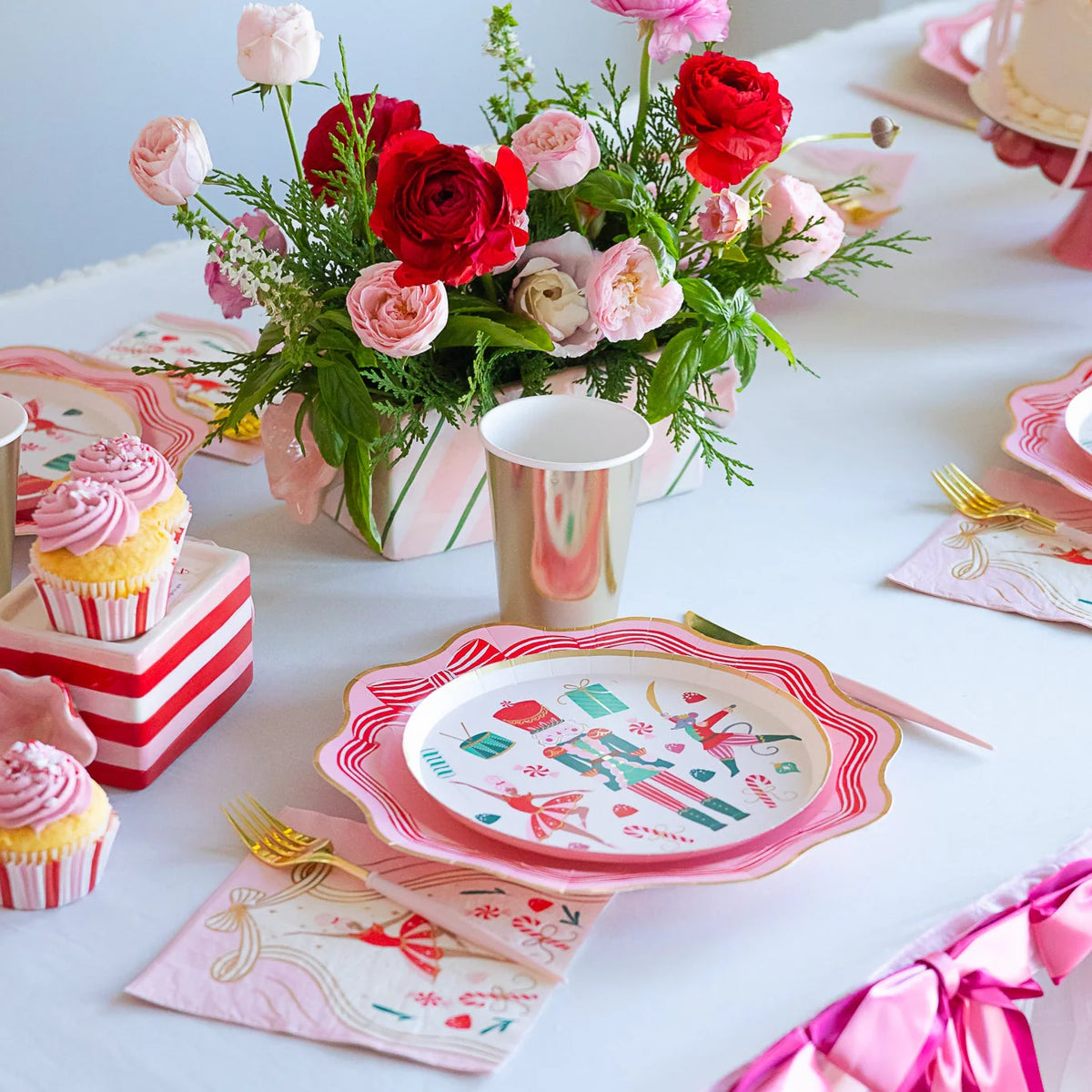 Table setting featuring pink Christmas decor plates, gold cups, and cupcakes, highlighting the ballet party supplies theme.