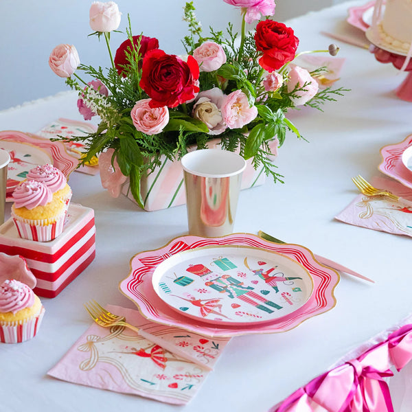 Table setting featuring pink Christmas decor plates, gold cups, and cupcakes, highlighting the ballet party supplies theme.