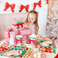 Child smiling beside Christmas setup with plaid cups and red bows