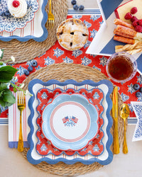 Overhead place setting with blue wave border dinner plate, scalloped dessert plate, and plaid stars cocktail napkin on woven charger