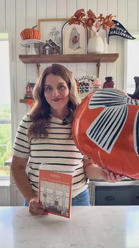 a woman holding the inflated pumpkin bow balloon in a styled Halloween kitchen with a garland and haunted house décor.
