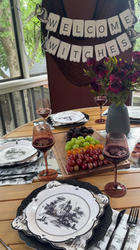 Halloween dinner table set with black and white toile haunted house plates, scalloped toile and black plates, fringed toile napkins, a toile table runner and a Welcome Witches banner