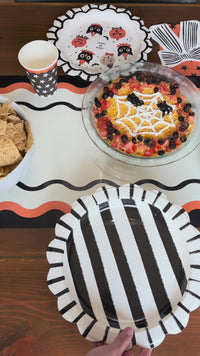 Black and cream sketchy striped Halloween paper plates with a scalloped edge, styled in a vintage Halloween tablescape as a charger under a pumpkin-shaped plate with a black bow napkin and Halloween icon plate