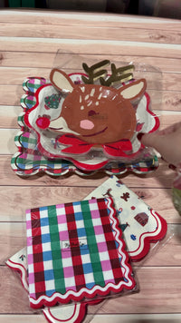 Christmas paper plates and napkins held up one at a time: plaid square plates, reindeer plates, Merry and Bright scalloped plates, guest napkins and plaid cocktail napkins