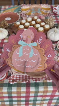 3D slot-together paper turkey craft with layered rust and orange feathers and a blue bow, shown with its flat pieces