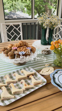 Panning video of a spring party tablescape anchored by a sage green striped paper table runner, layered underneath floral paper dinner plates, gold flatware, and pastel drinking cups.