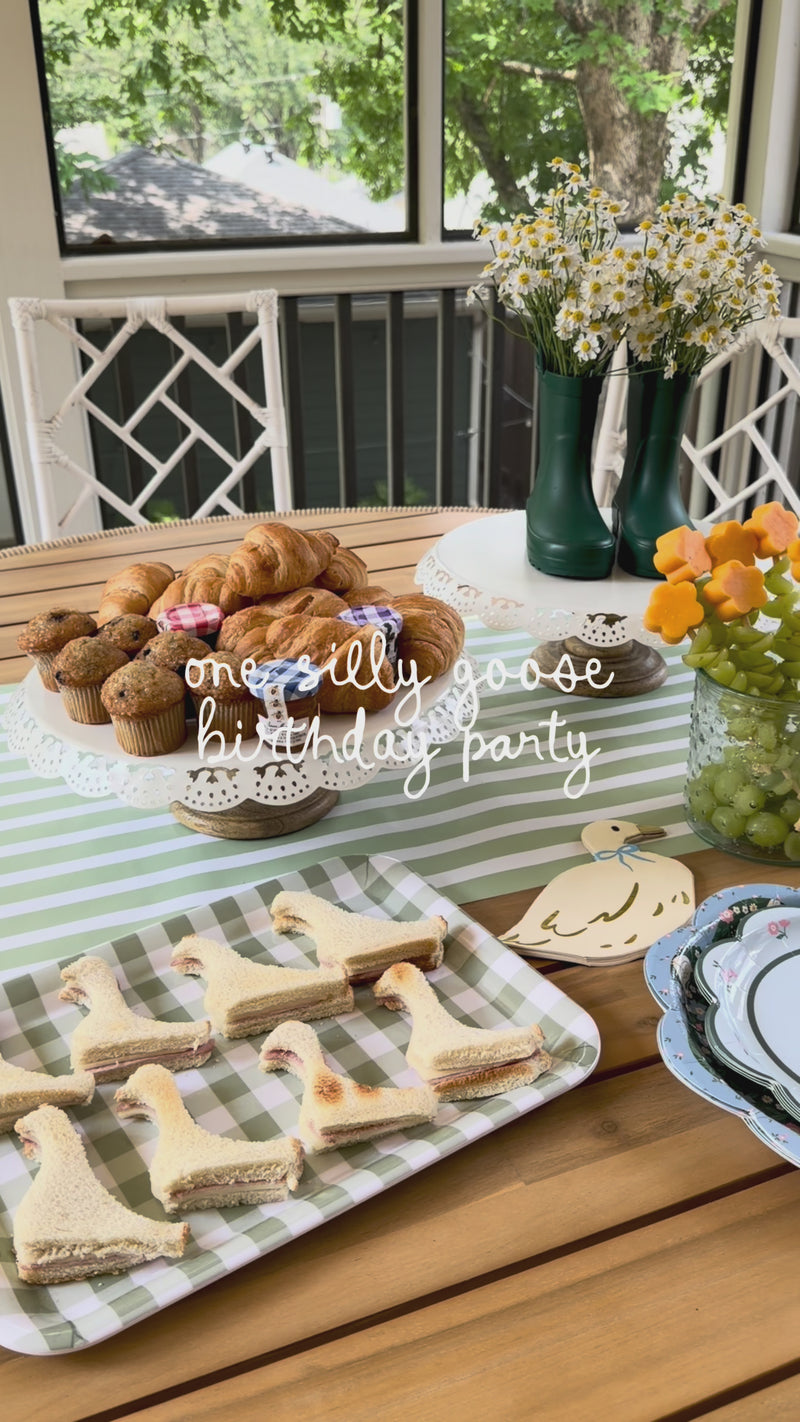 Panning video of a spring party tablescape anchored by a sage green striped paper table runner, layered underneath floral paper dinner plates, gold flatware, and pastel drinking cups.