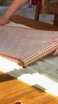 Person setting a Thanksgiving table with fall leaf turkey plates, orange gingham scalloped plates, a gingham floral table runner, pumpkin napkins and gingham napkins