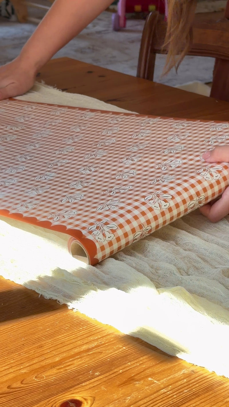 Person setting a Thanksgiving table with fall leaf turkey plates, orange gingham scalloped plates, a gingham floral table runner, pumpkin napkins and gingham napkins
