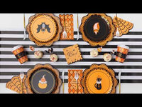 Close-up video of the Harlequin Halloween pumpkin-shaped paper plates turning to show the orange and marigold argyle pattern, black diamond lines, and black stem, styled with black pumpkins and fall décor.