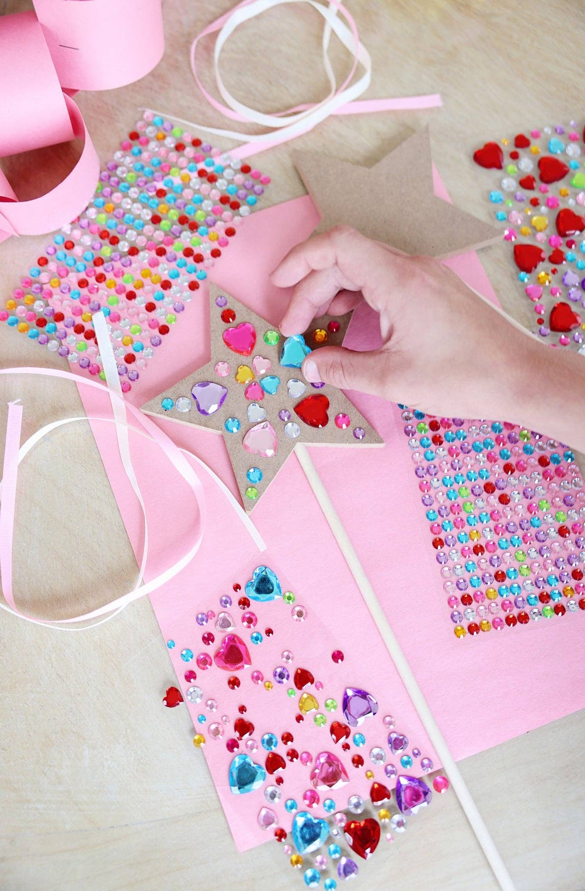 A child's hand placing heart-shaped gems on a Customizable Fairy Wand as part of a Birthday Party Craft Station.