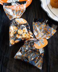 Clear bags with orange and black polka dots containing Halloween-themed treats on a dark surface with black baker's twine.
