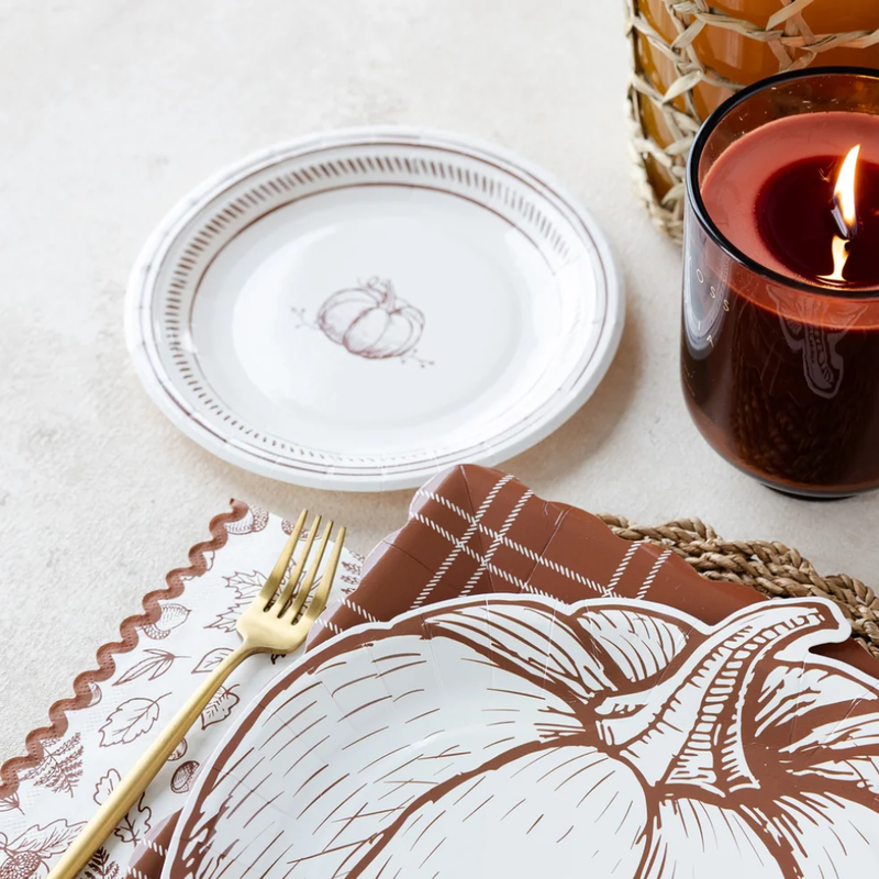 A close-up of a fall table setting with a pumpkin-shaped plate, gold flatware, and a lit candle.