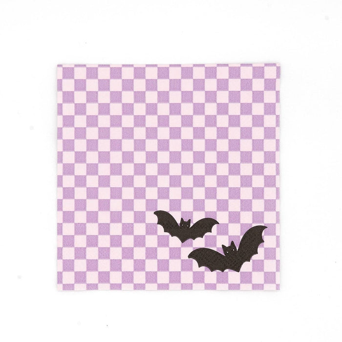 Purple checkered paper cocktail napkin with two black bats printed in the lower corner, shown flat on white