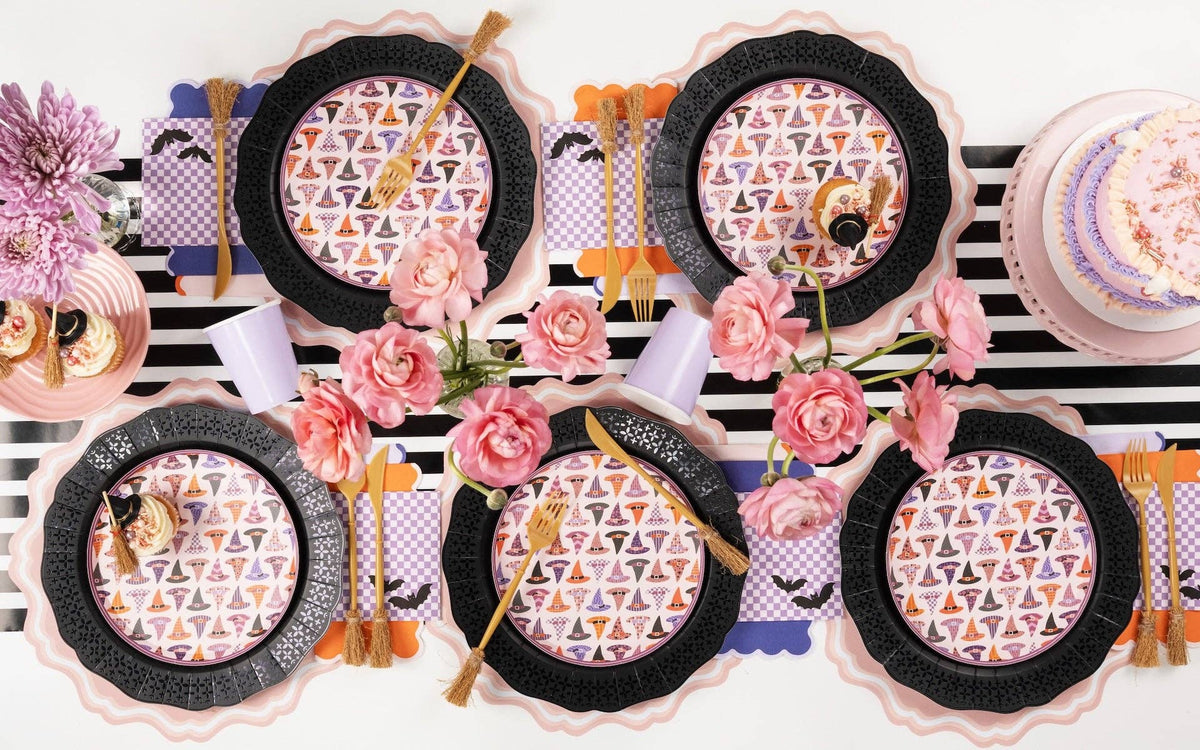 Overhead Halloween tablescape with purple bat cocktail napkins, witch hat plates, black scalloped chargers and pink ranunculus