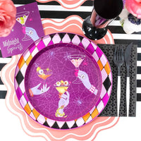Styled purple Halloween cocktail party table — purple plates with cocktail illustrations, pink and orange harlequin accents, pink roses, and the black foil guest towels.